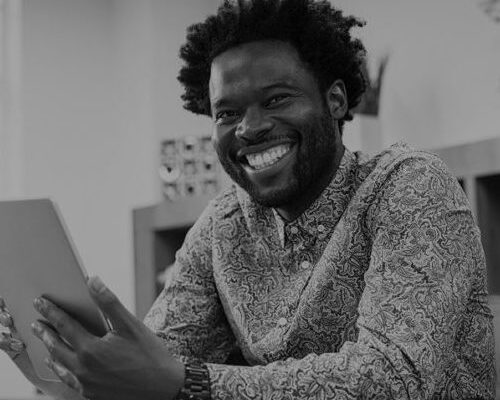 Happy casual african man using digital tablet at office. Portrait of smiling black businessman sitting on chair using tablet pc. African american casual business man looking at camera.