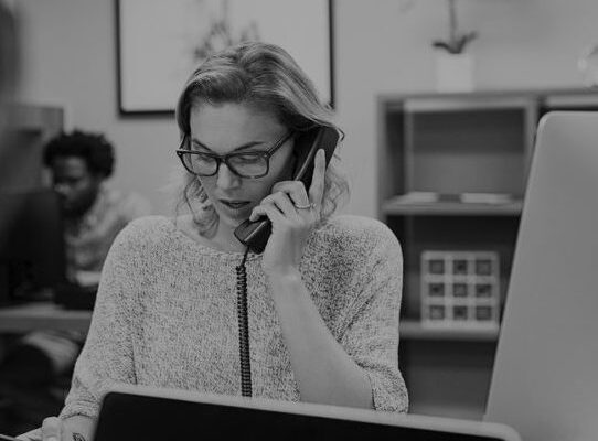 Mature businesswoman talking on phone in office. Casual business woman talking on landline phone in a creative agency. Beautiful blonde receptionist with eyeglasses taking client details over phone.