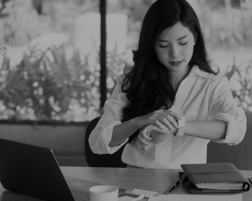 asian businesswoman look at her watch at workplace. startup woman check time on wristwatch at office. young female entrepreneur with paperwork on table.